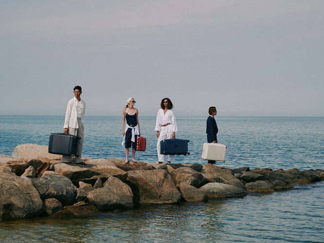 a group of people with luggage on rocks by water