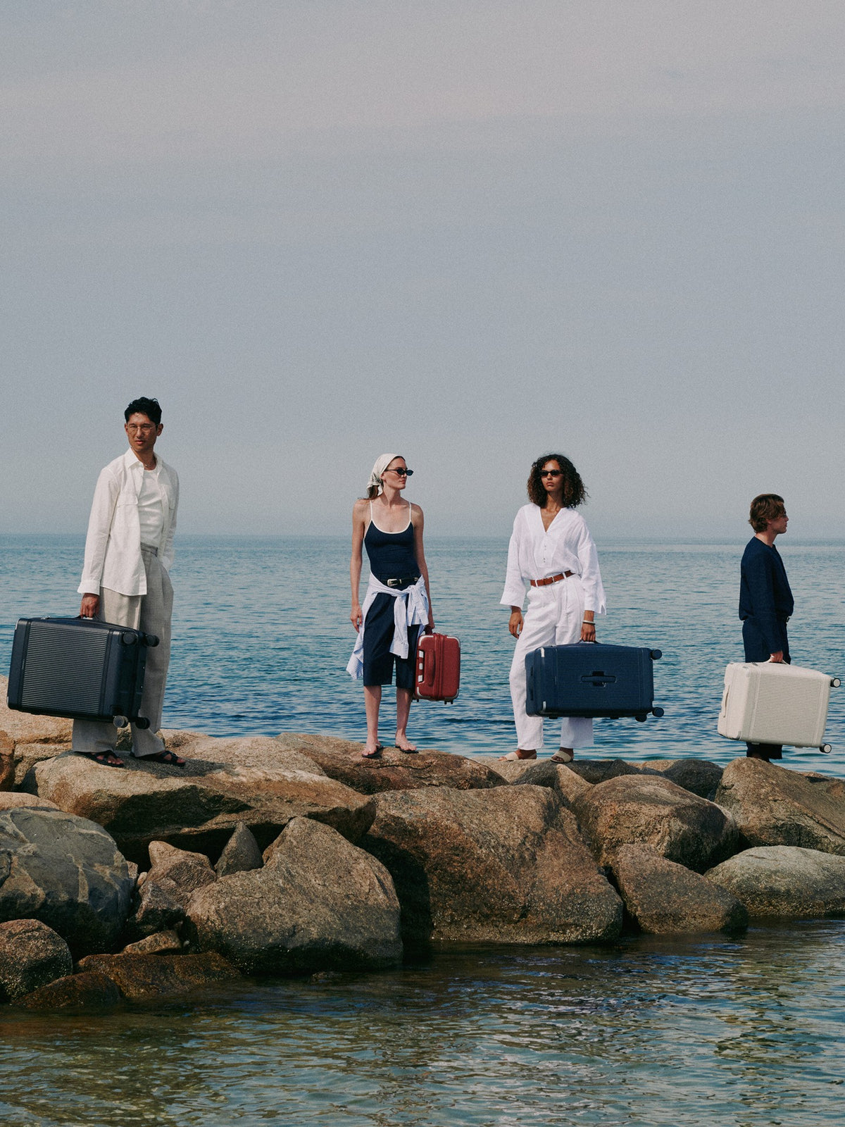a group of people holding luggage on rocks by water