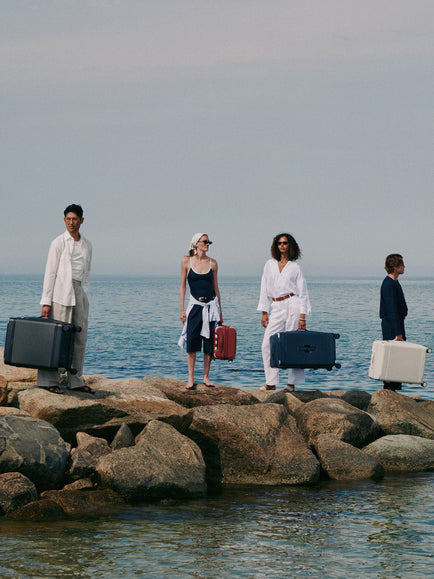 a group of people holding luggage on rocks by water